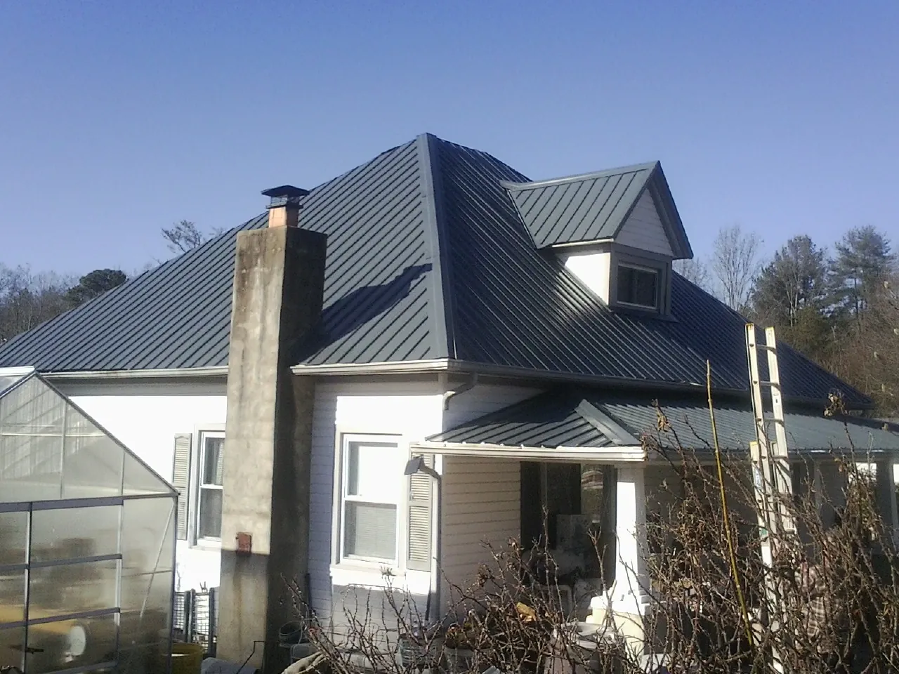 Dark blue standing seam metal roof on a white farmhouse with dormer — Slate & Tile Roof Repair by Roofing Brothers in Southern Pines