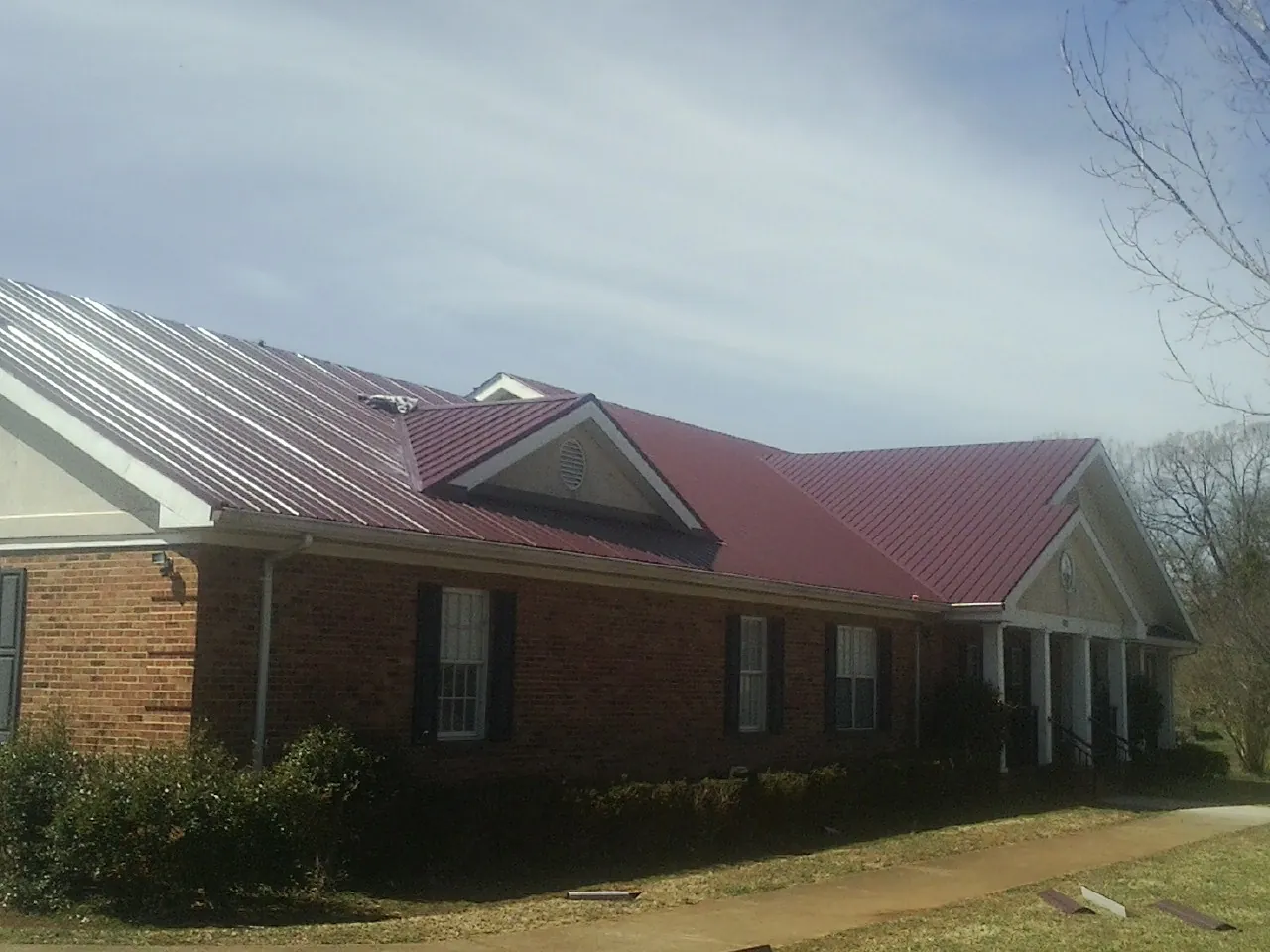Red metal roof with gabled entries on a long brick building, from a Hail Damage Roof Repair job in Southern Pines