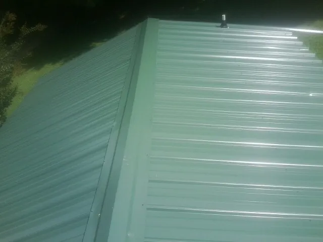New green metal panels meeting at the ridge of a roof — Flat Roof Repair work by our crew in Southern Pines