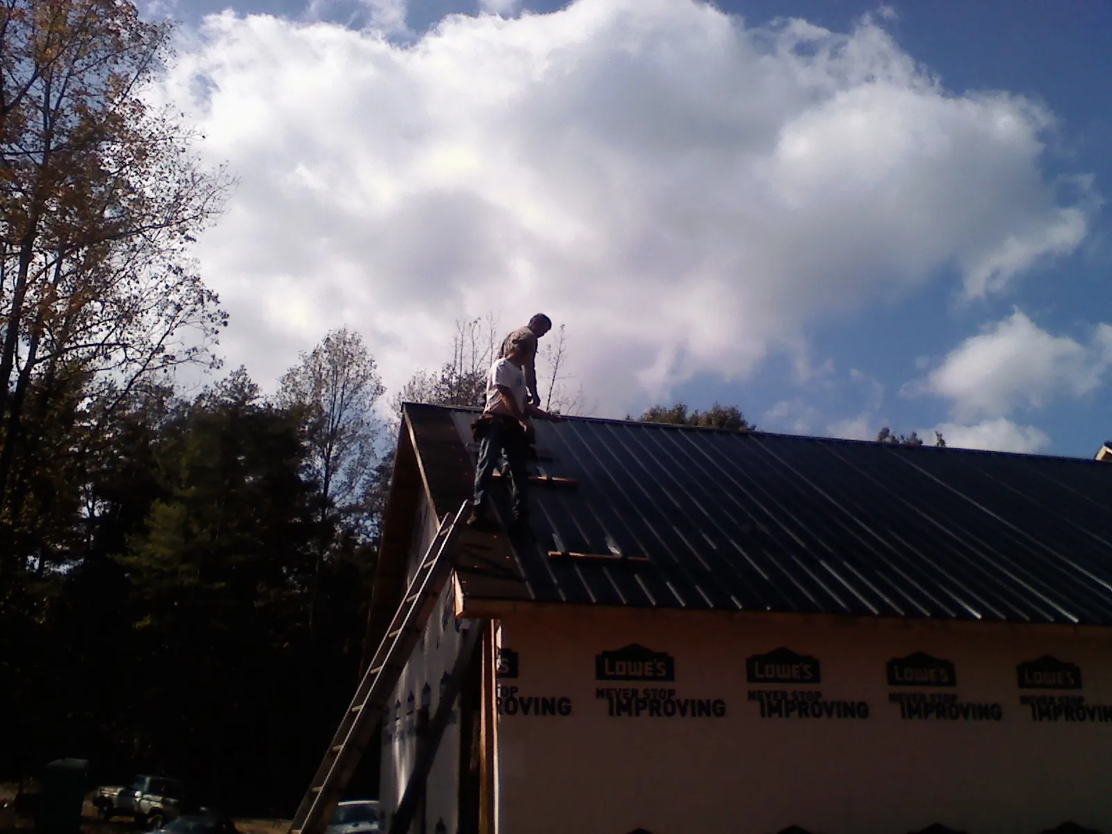 Roofer fastening dark metal panels high against a cloudy sky, from a Roof Inspection job in Southern Pines