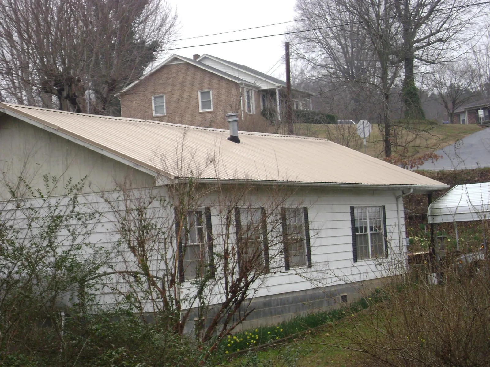Tan metal roof on a white sided house set into a hillside — Commercial Roofing by Roofing Brothers in Southern Pines