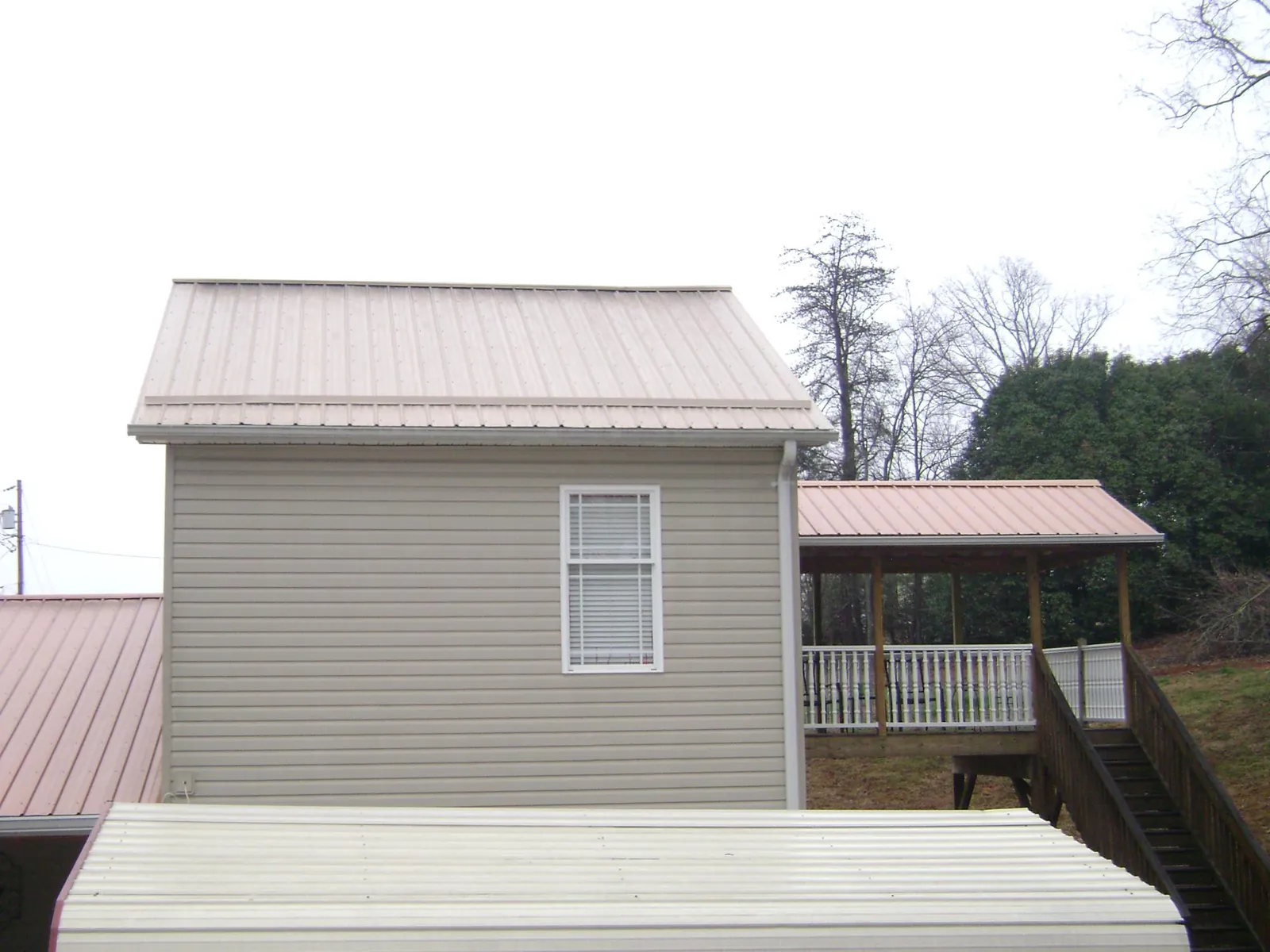 Tan metal roofs on a two story addition and attached porch, from a Roof Replacement job in Southern Pines